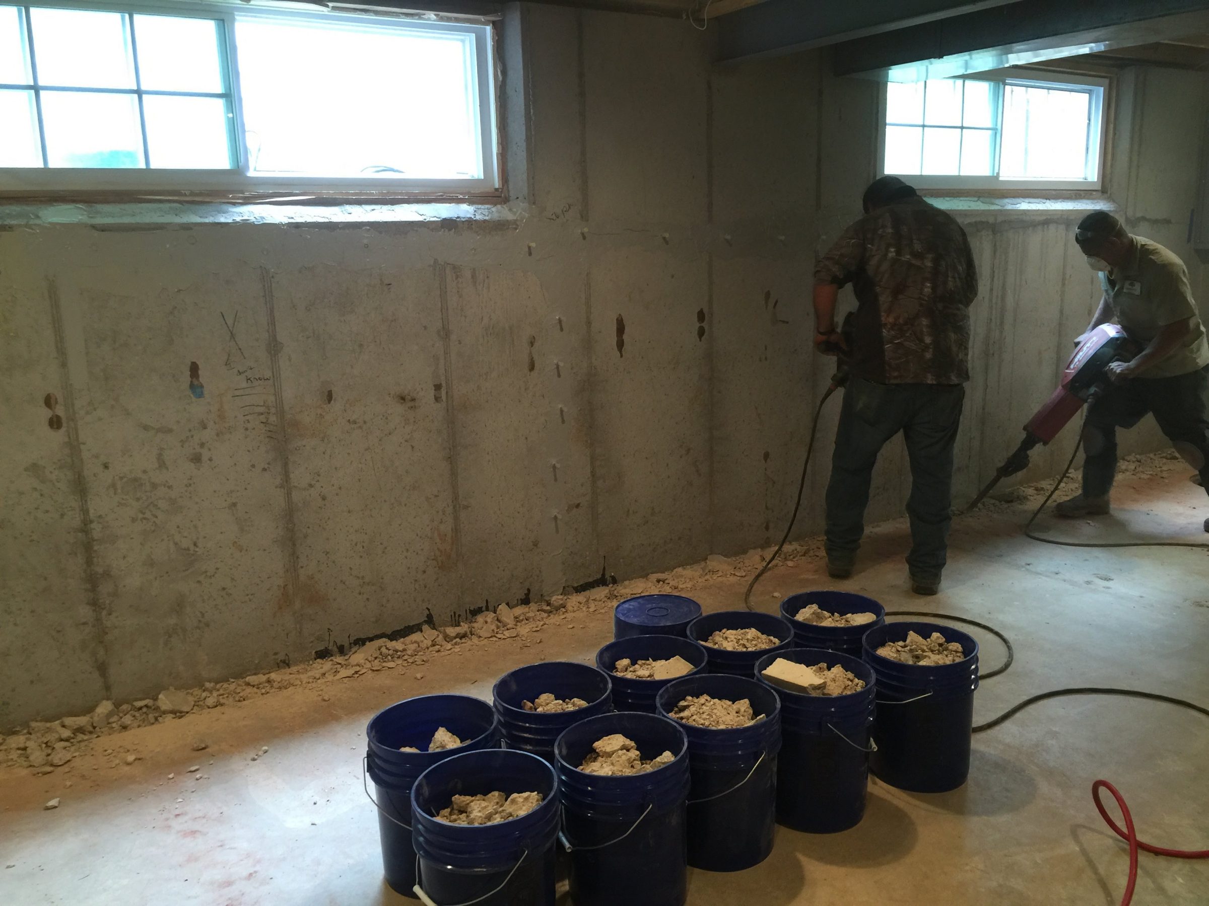 Workers removing concrete from basement wall with jackhammer