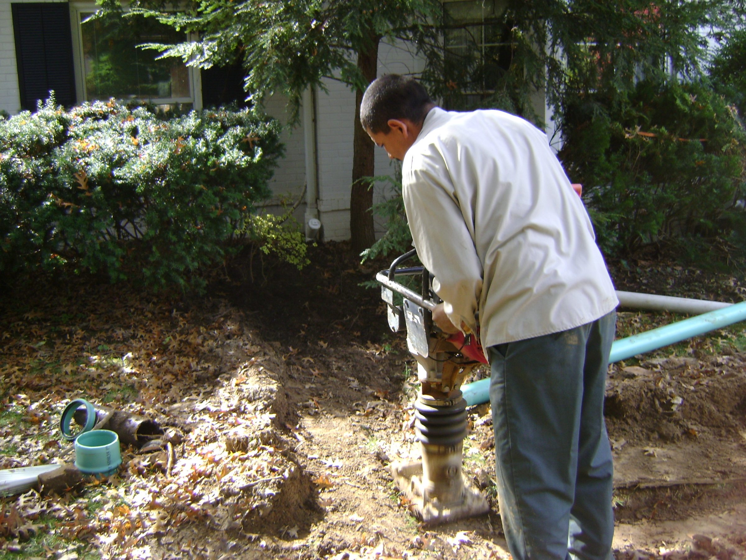 Man using soil compactor in backyard trench