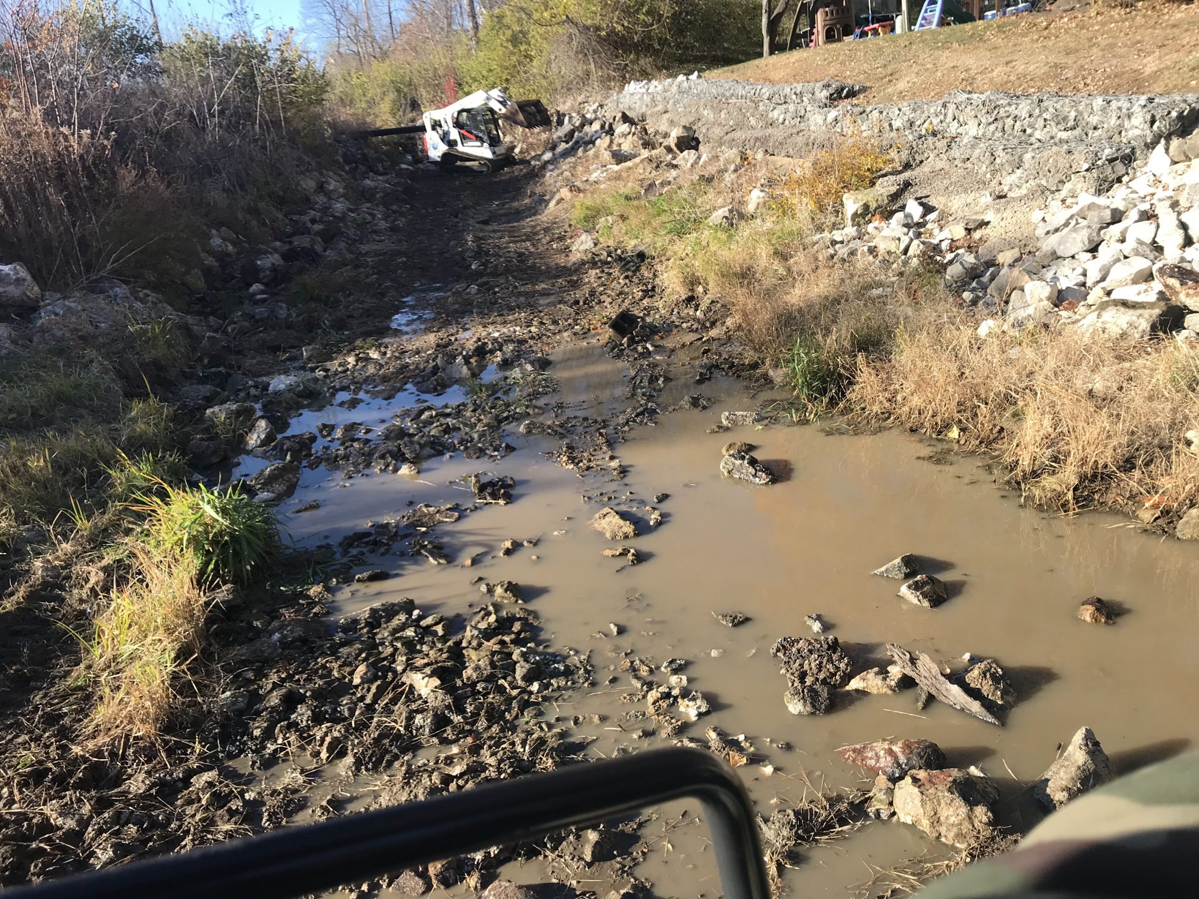 Skid-steer loader in muddy drainage ditch