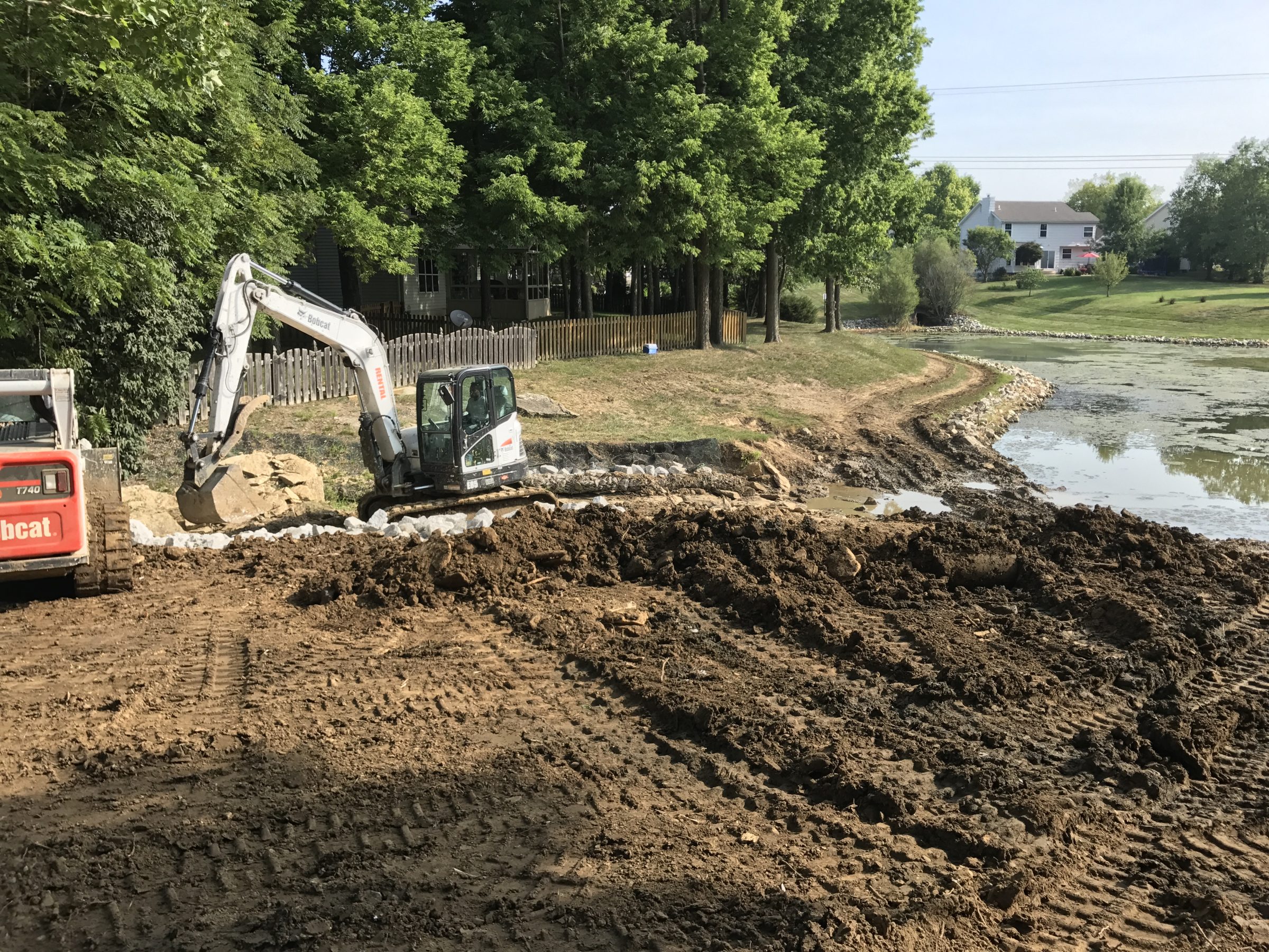 Excavator reinforcing pond shoreline in residential neighborhood