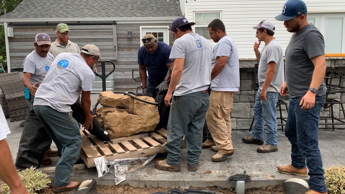 Workers moving large rocks onto backyard patio