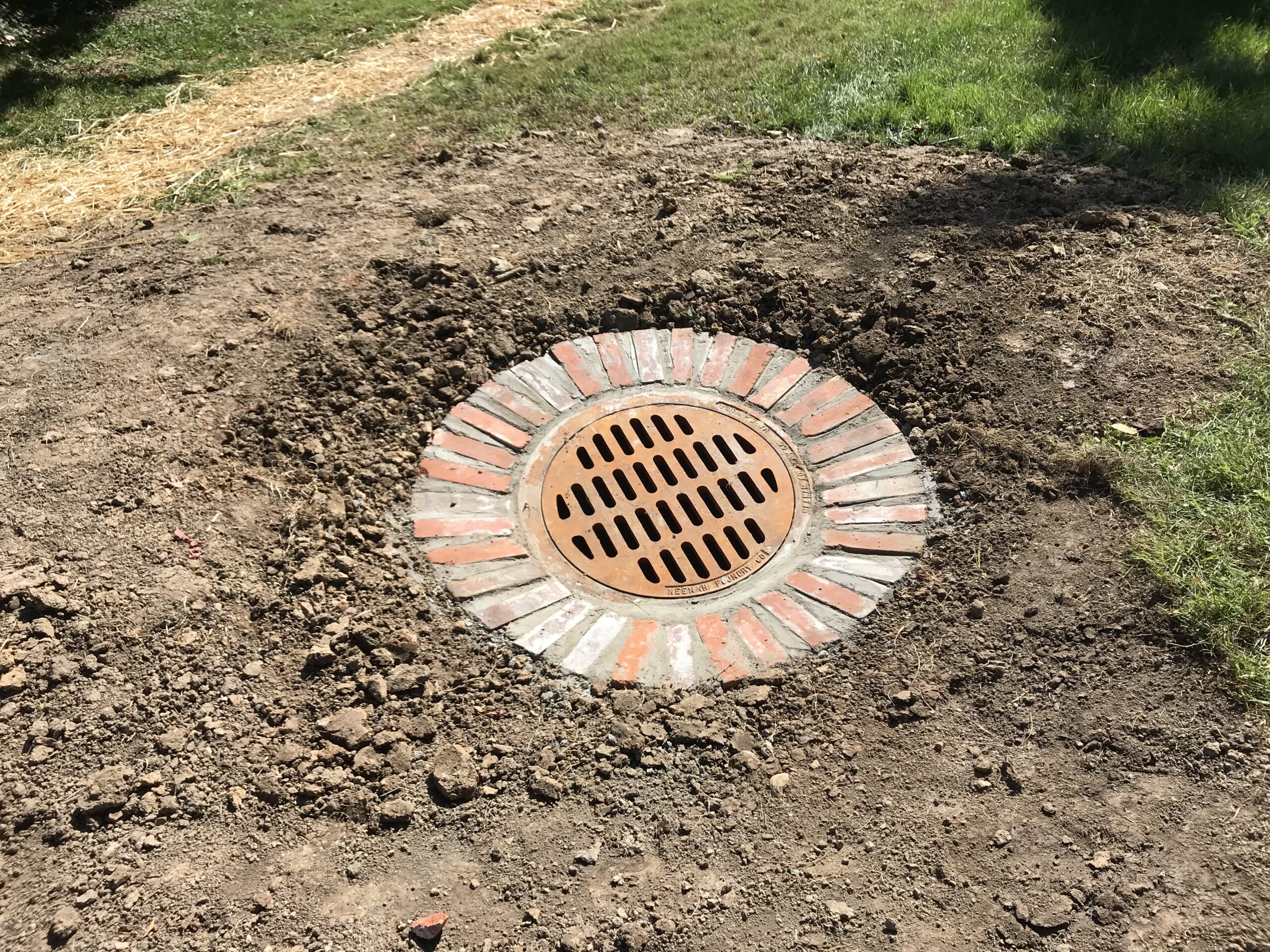 Circular storm drain with brick surround in dirt