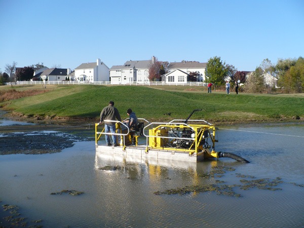 Workers operating small dredging machine in pond
