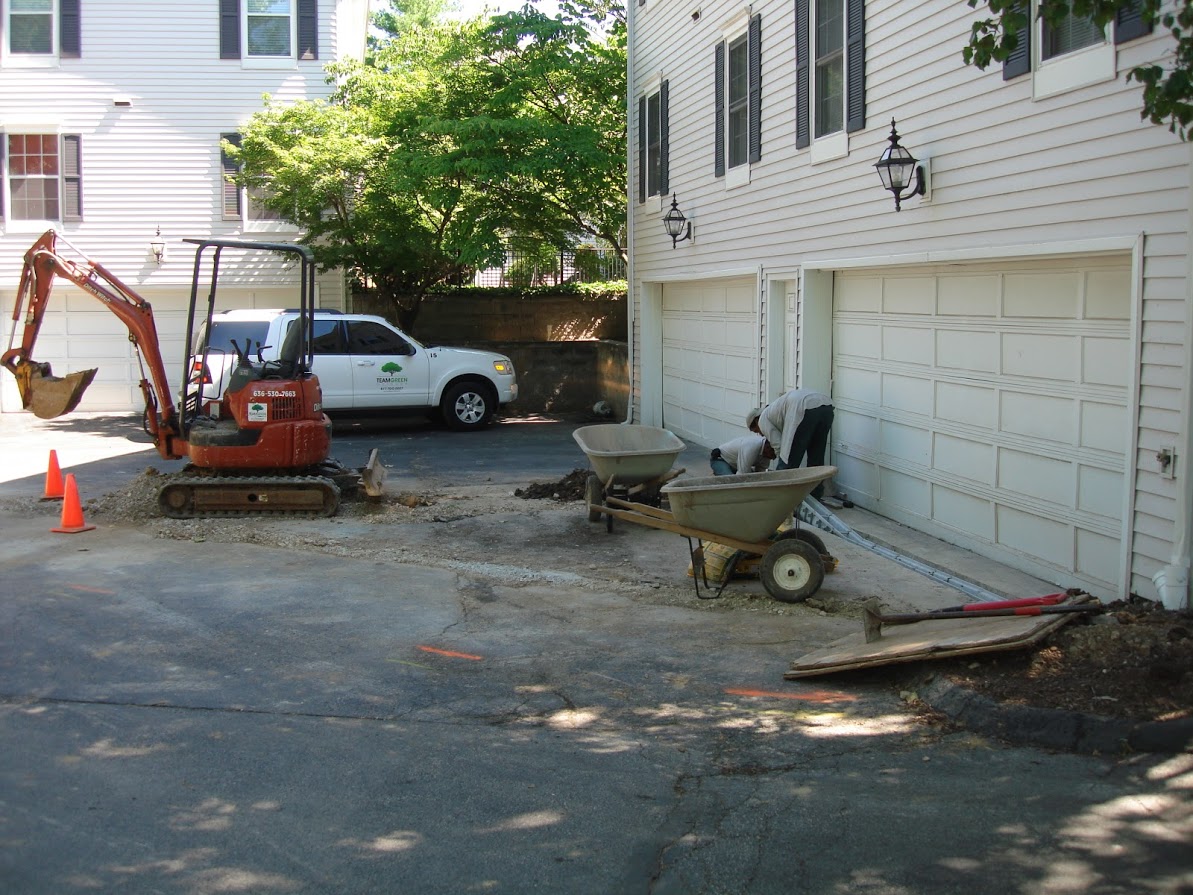 Excavator and workers repairing residential driveway