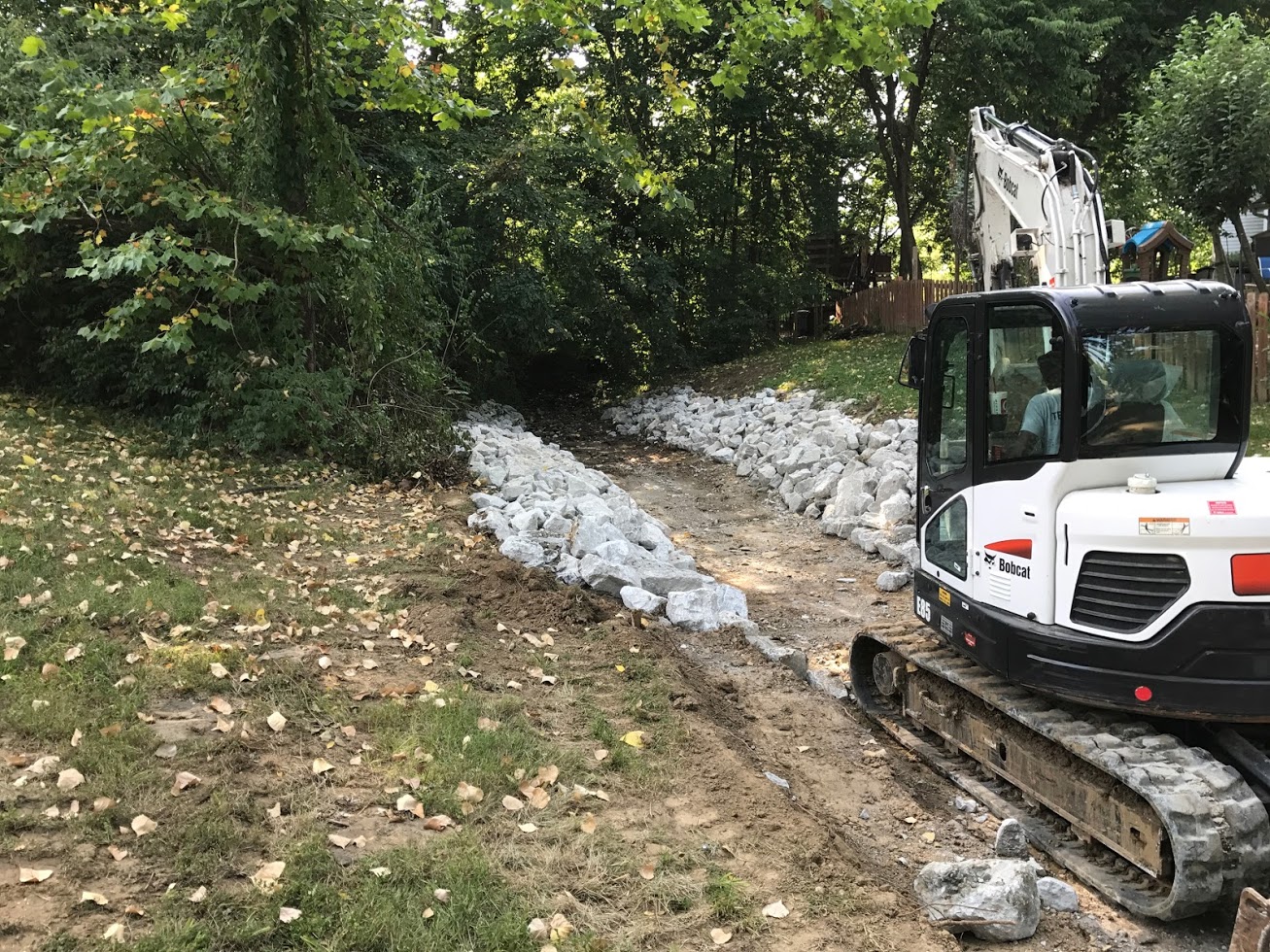 Excavator lining drainage ditch with white rocks
