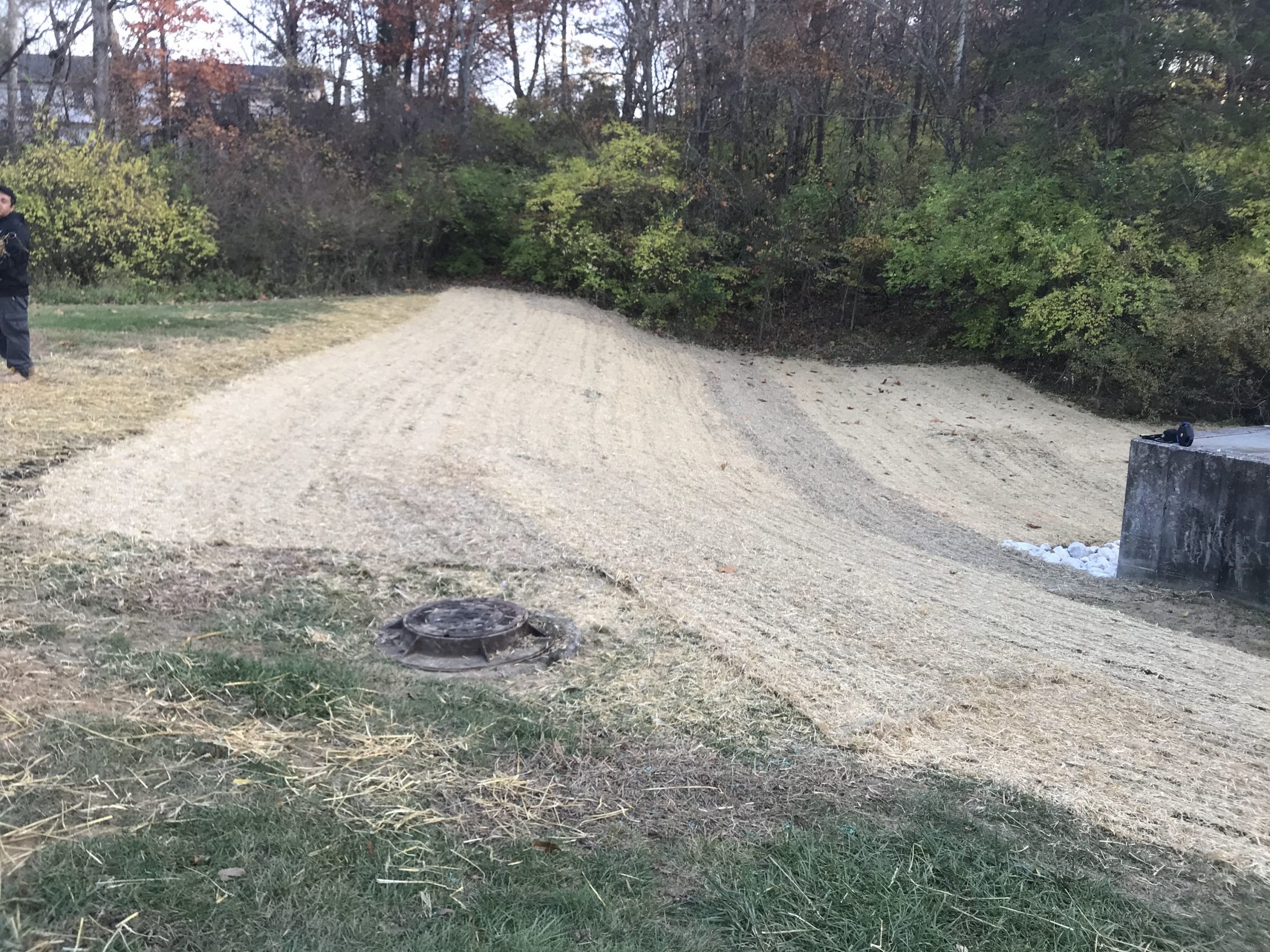 Freshly graded embankment with manhole cover and trees