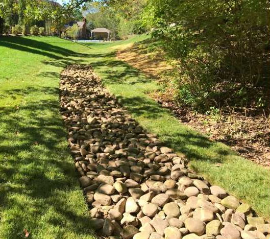 Rock-lined dry creek bed in grassy yard