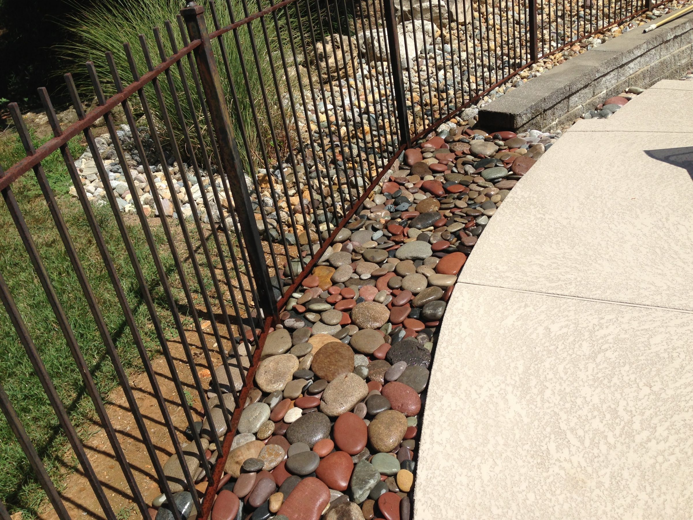 Curved metal fence beside landscaped river rocks