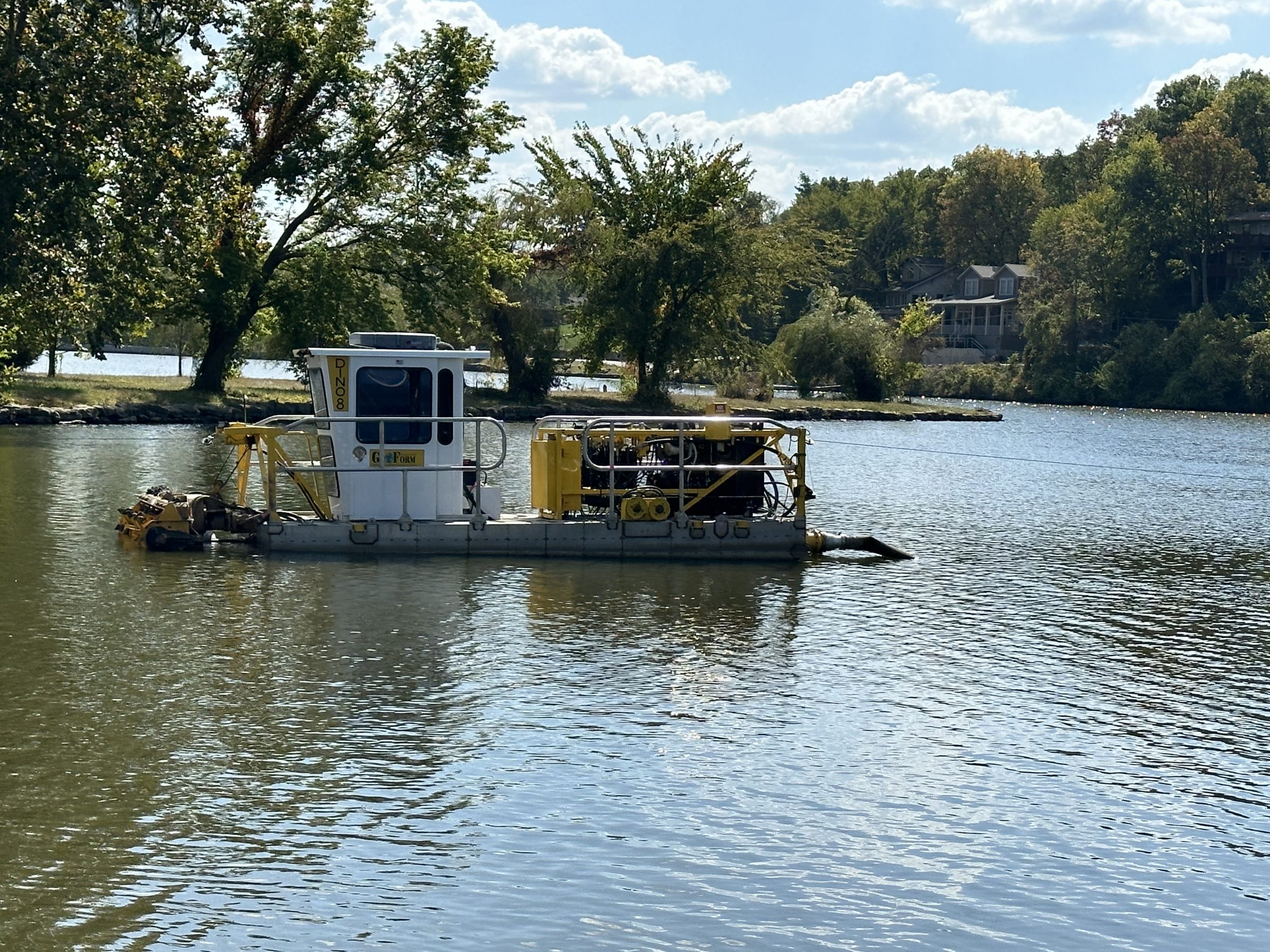 Small dredging boat on calm river near trees