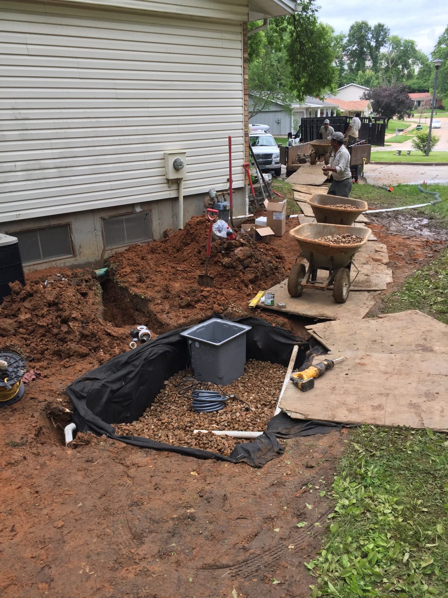 Workers installing drainage system beside house foundation
