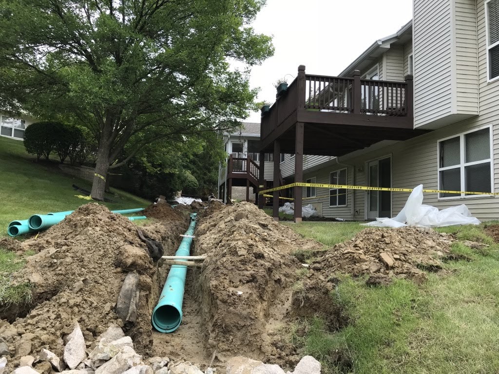 Trench with green pipes beside apartment building