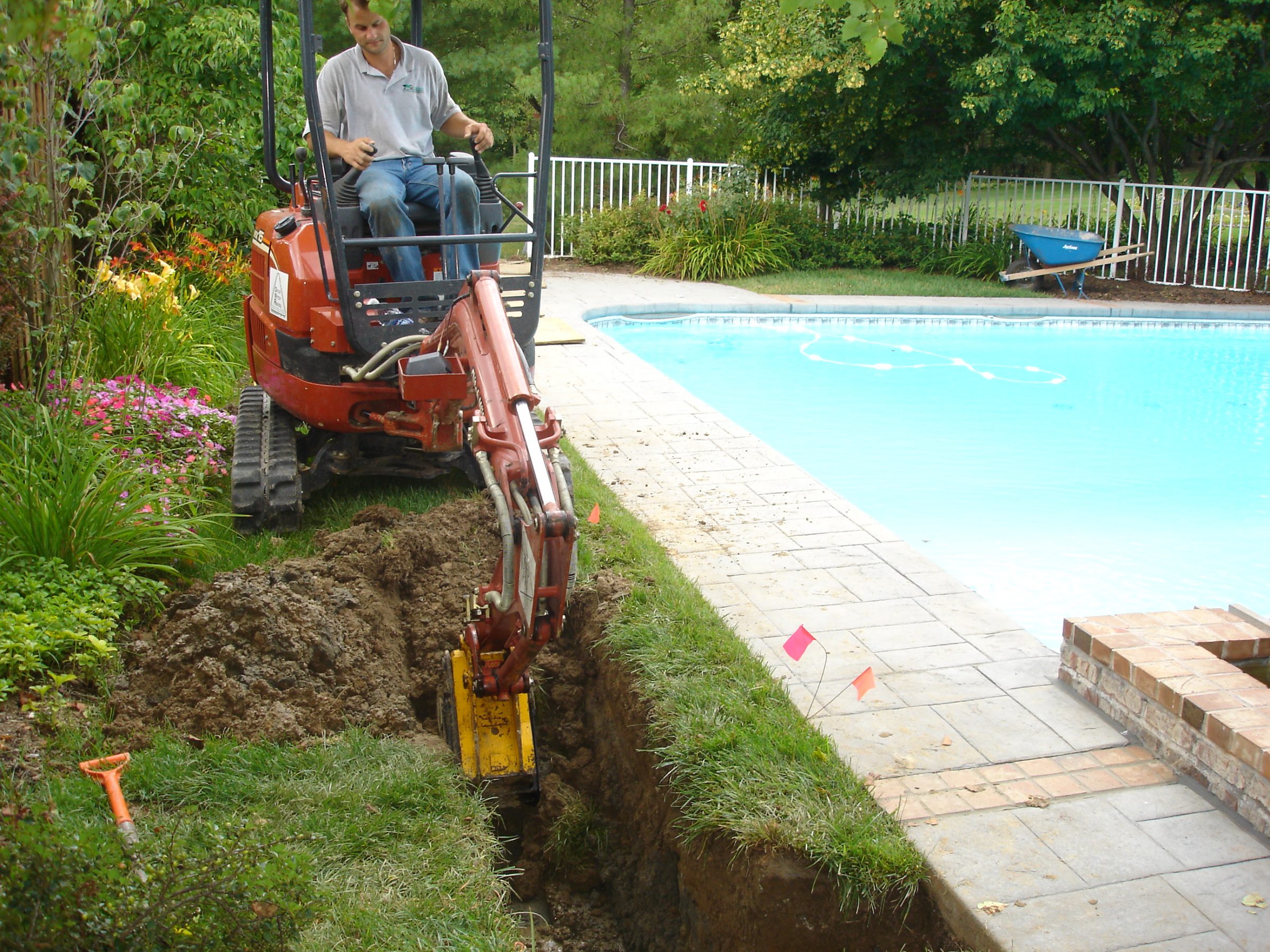 Worker digging trench beside backyard swimming pool
