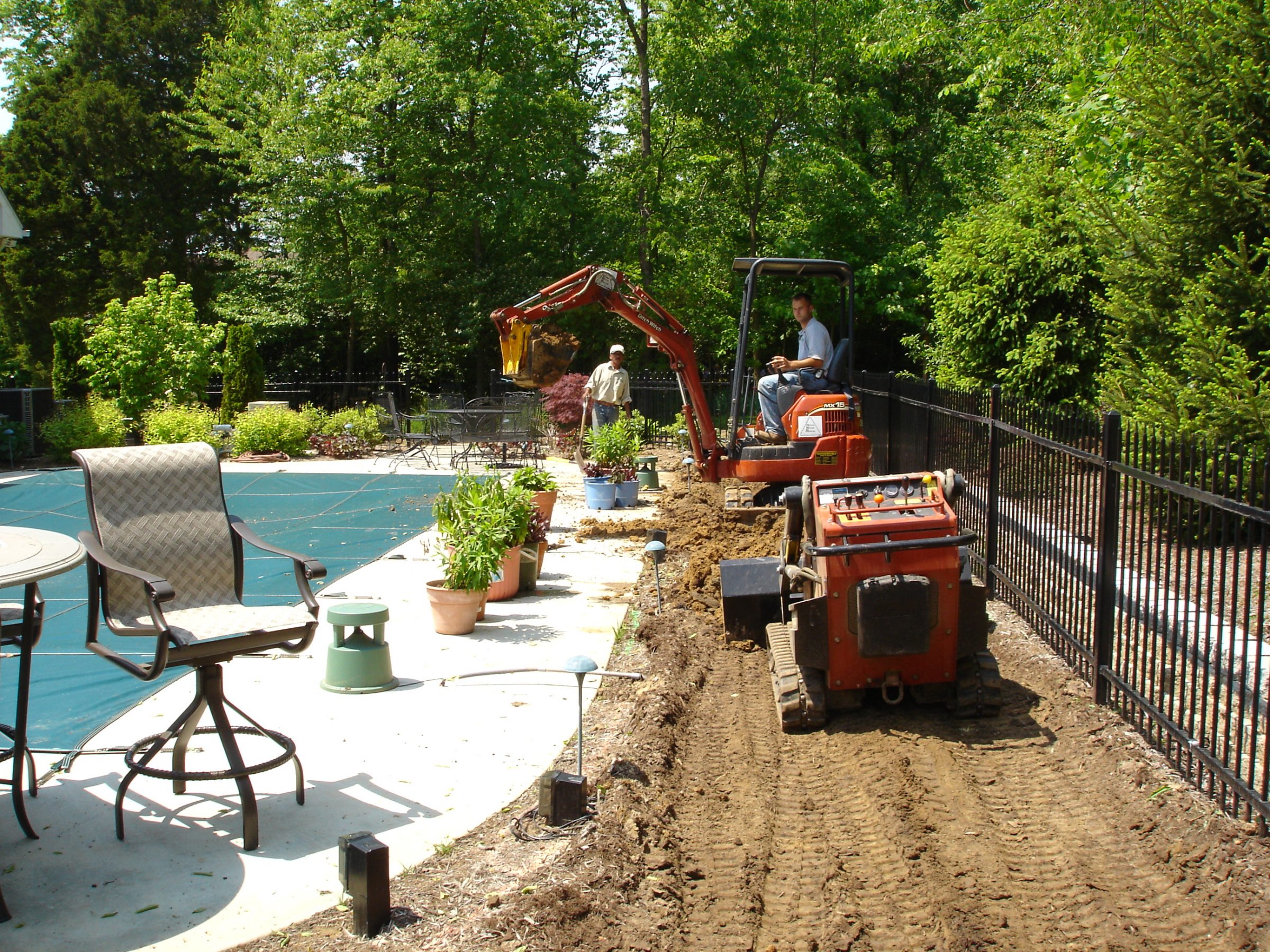 Mini excavator digging trench beside backyard pool