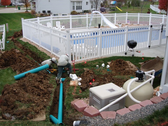 Workers installing underground pipes near backyard pool