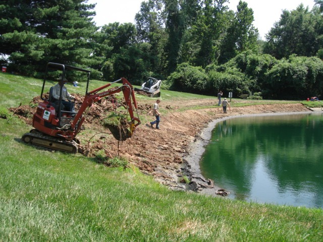 Excavator digging near pond shoreline with workers