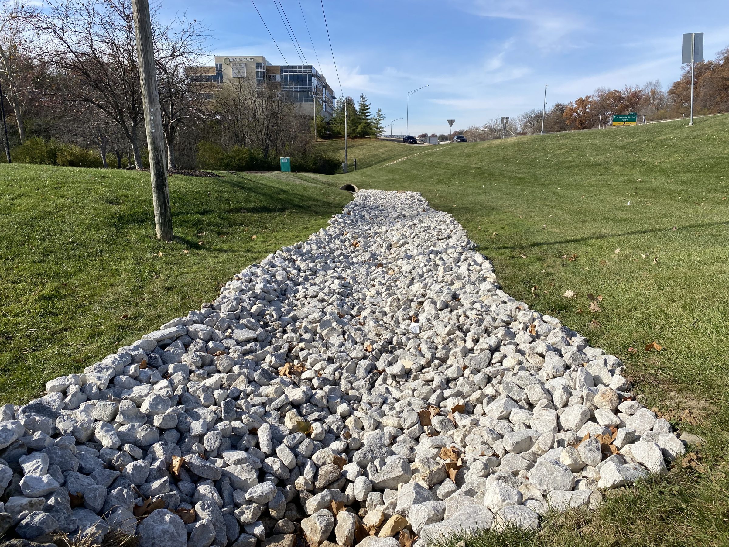Rock-filled drainage ditch beside grassy roadside slope