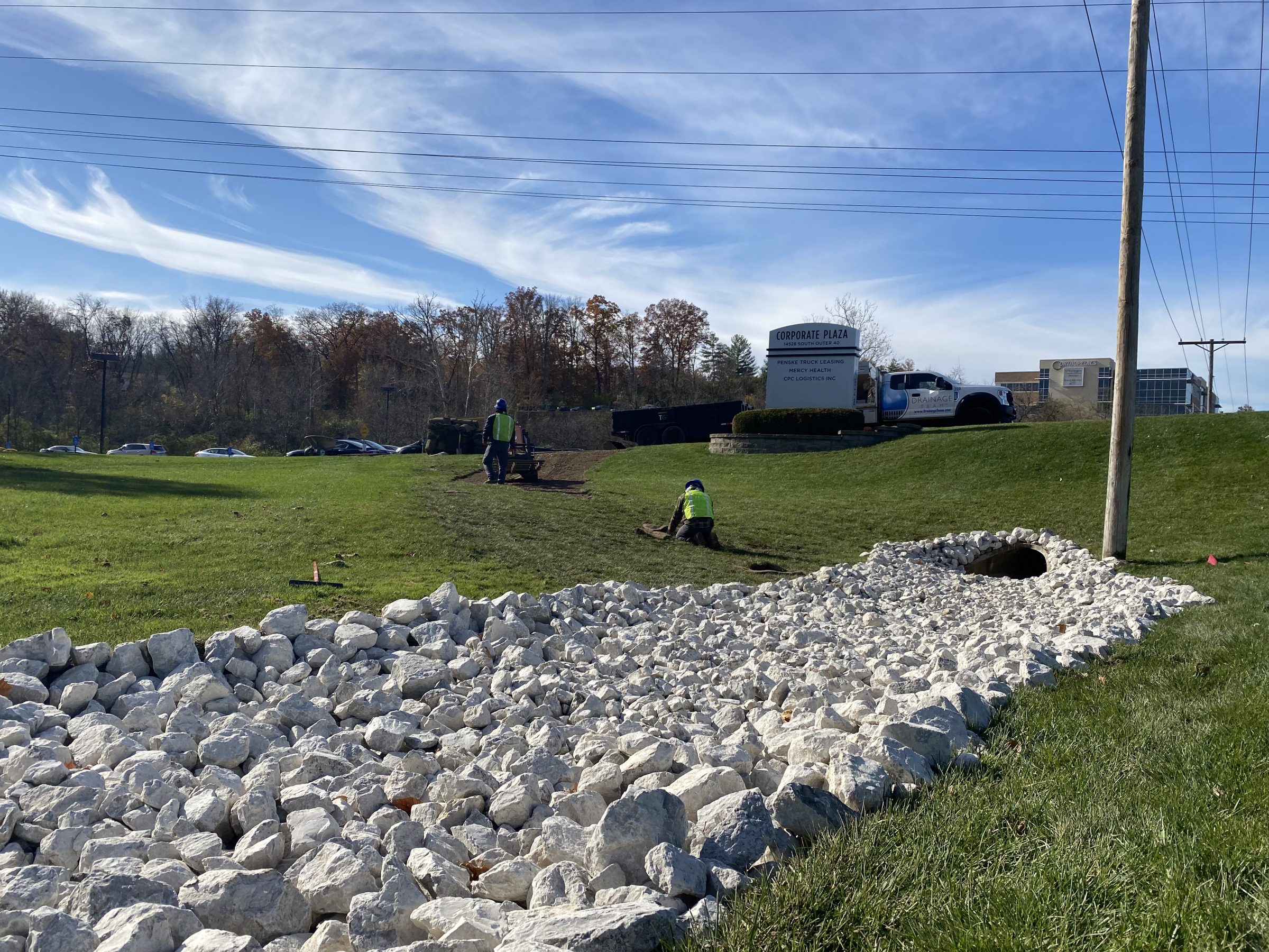 Workers installing drainage rocks on grassy slope
