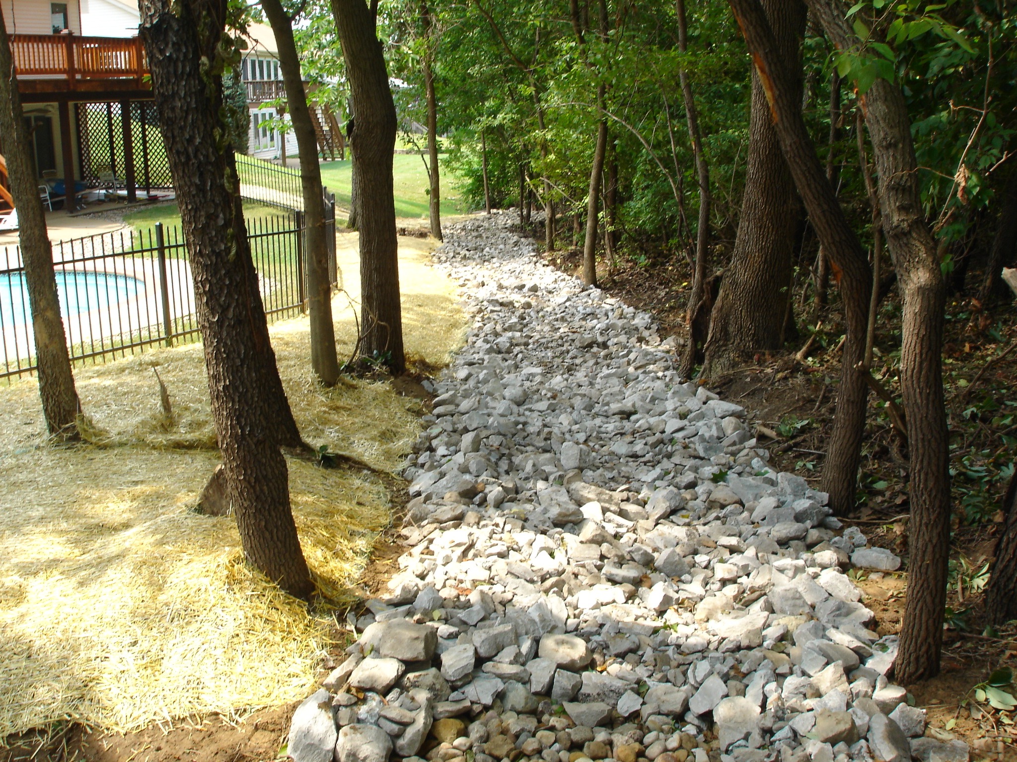 Rock-lined drainage ditch beside wooded backyard