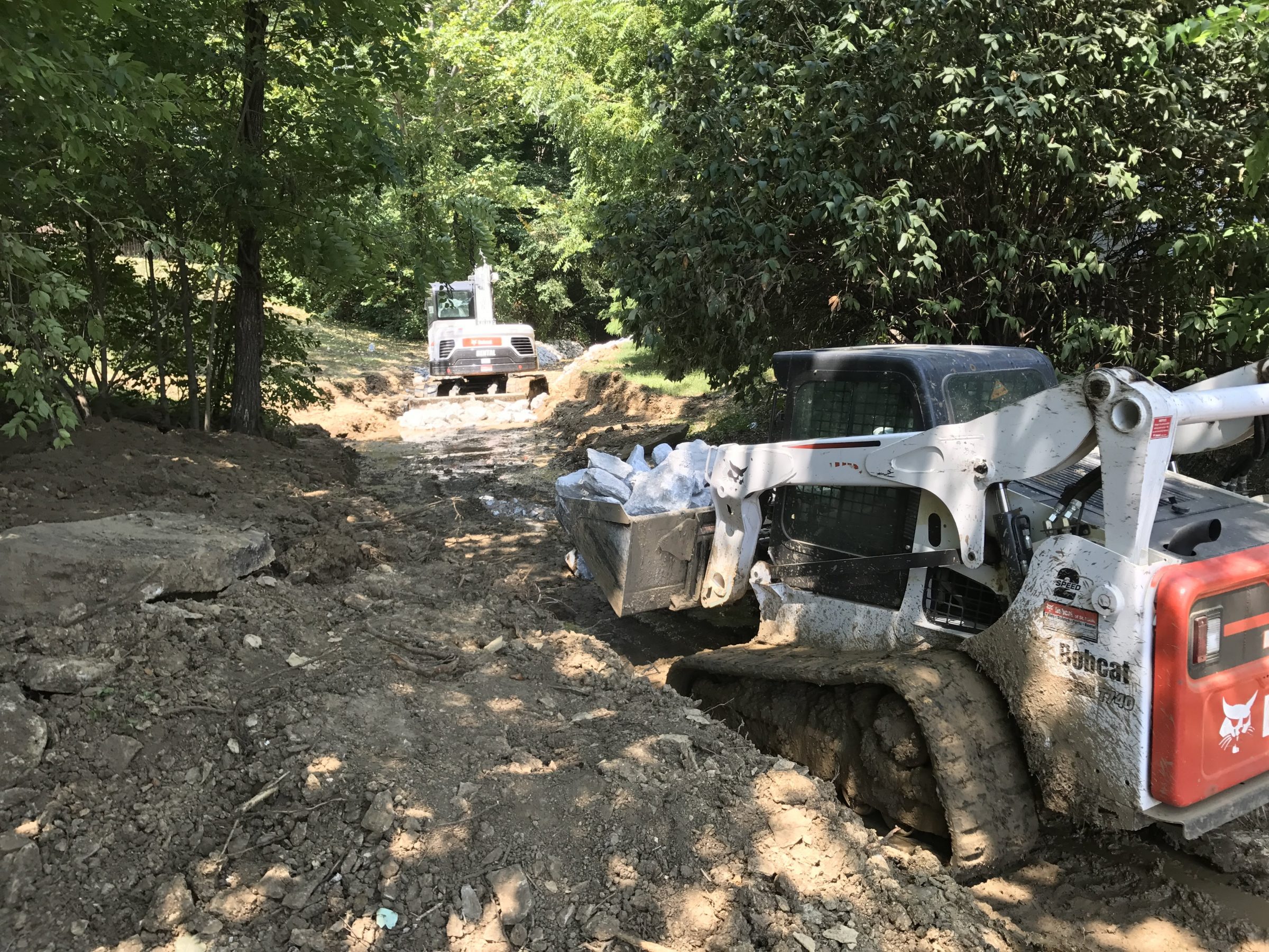 Skid-steer loaders grading dirt path in woods