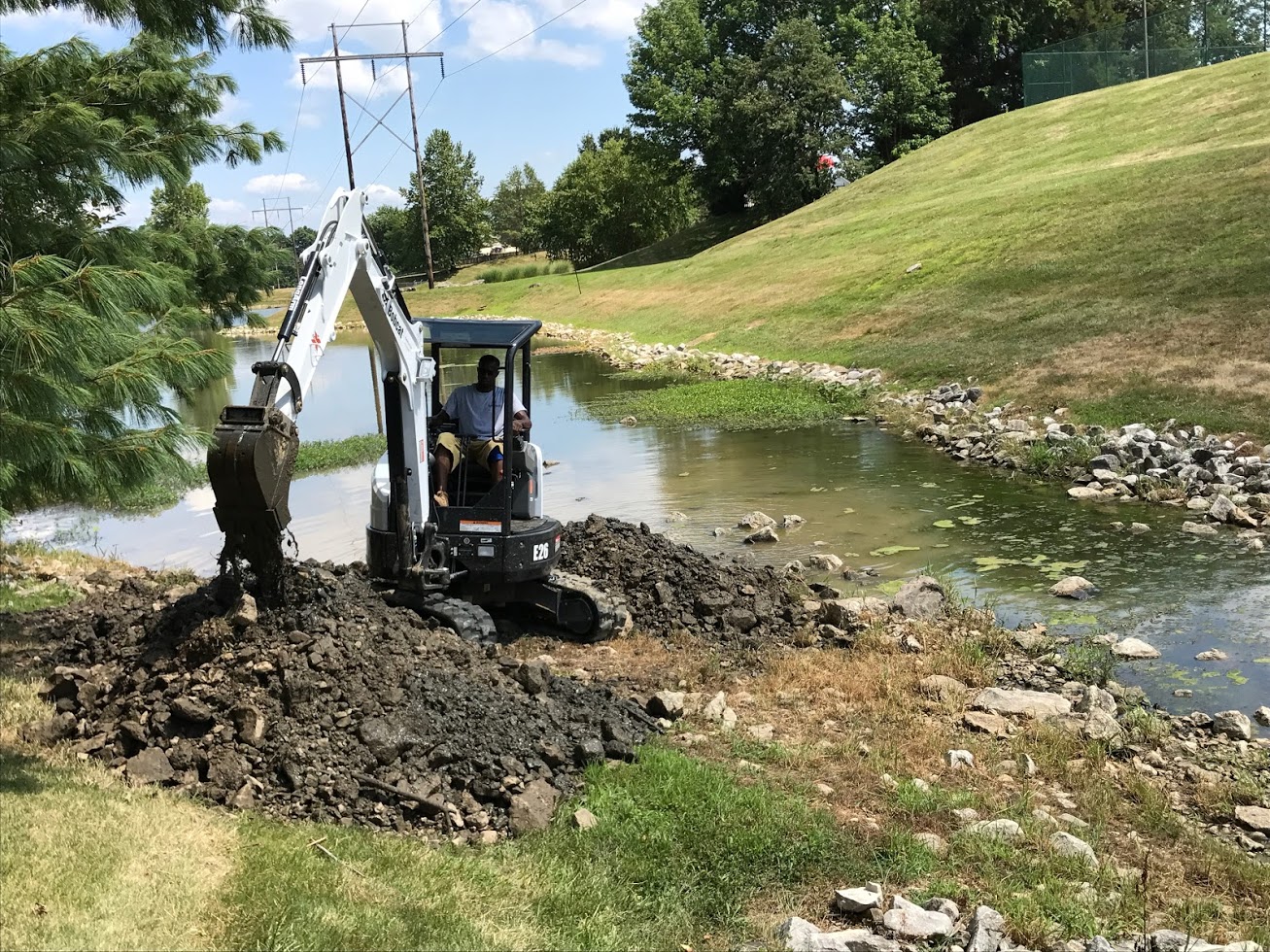 Mini excavator digging beside grassy pond bank