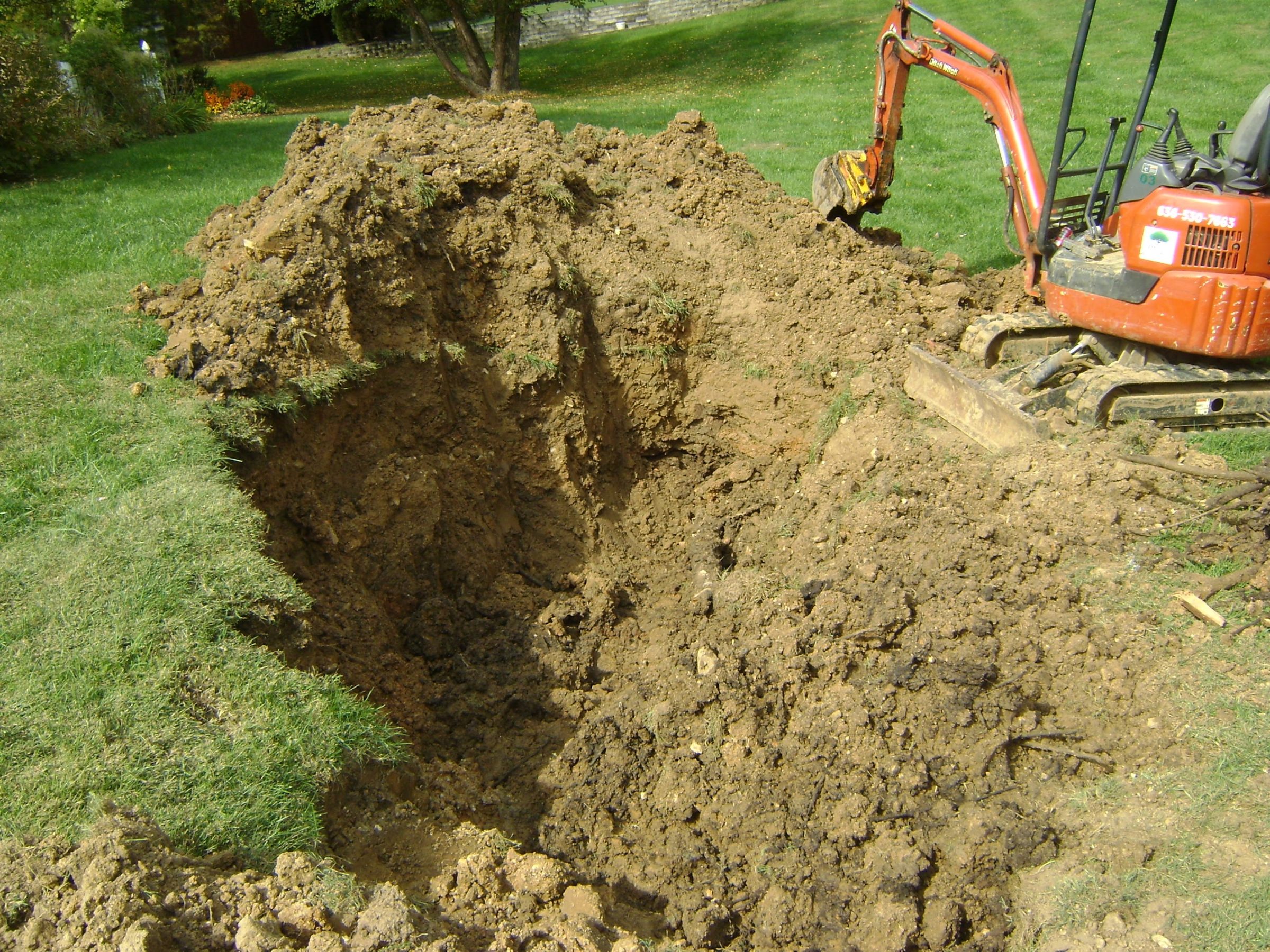 Mini excavator digging deep trench in grassy yard