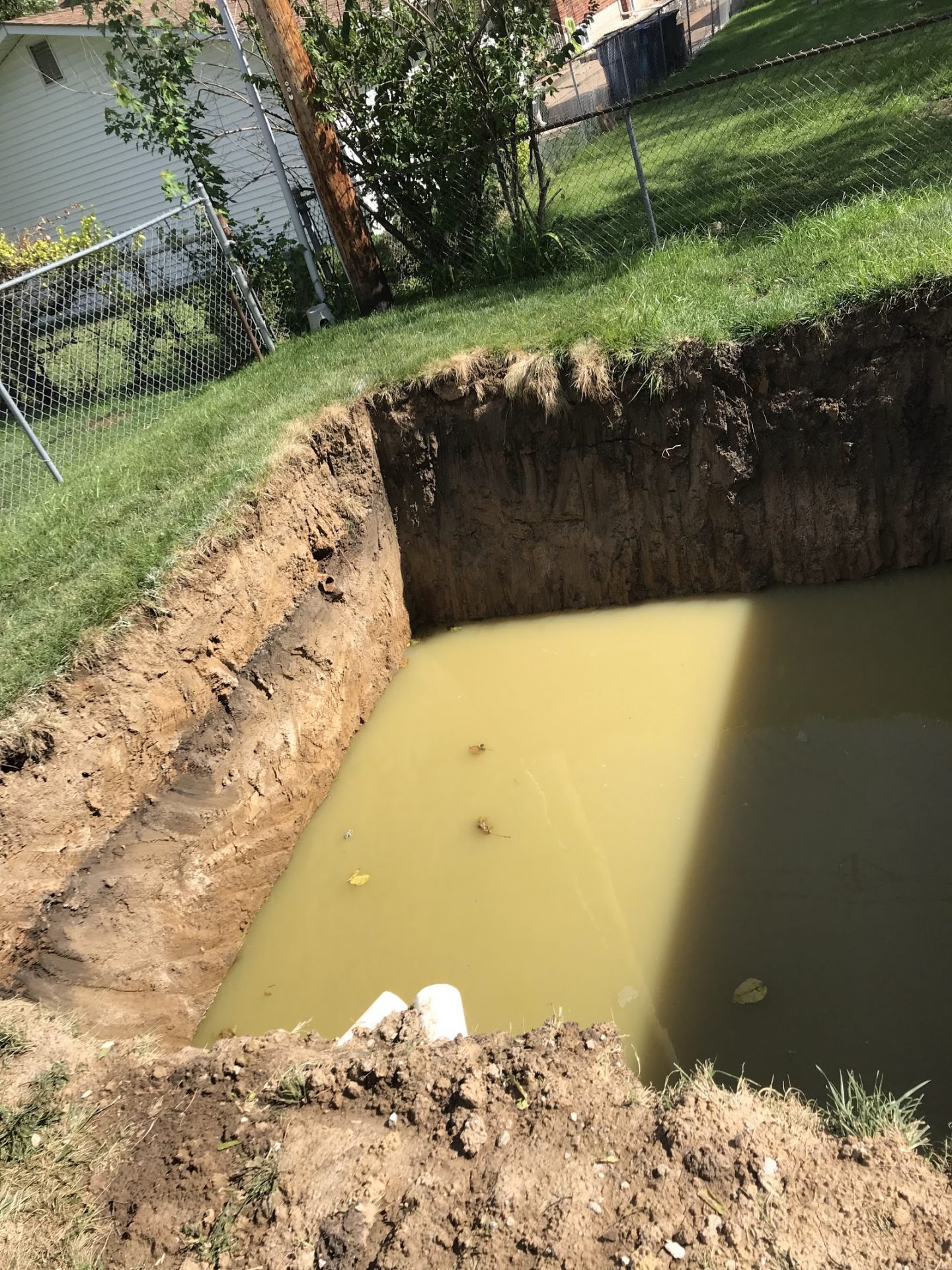 Large muddy excavation hole in backyard near fence