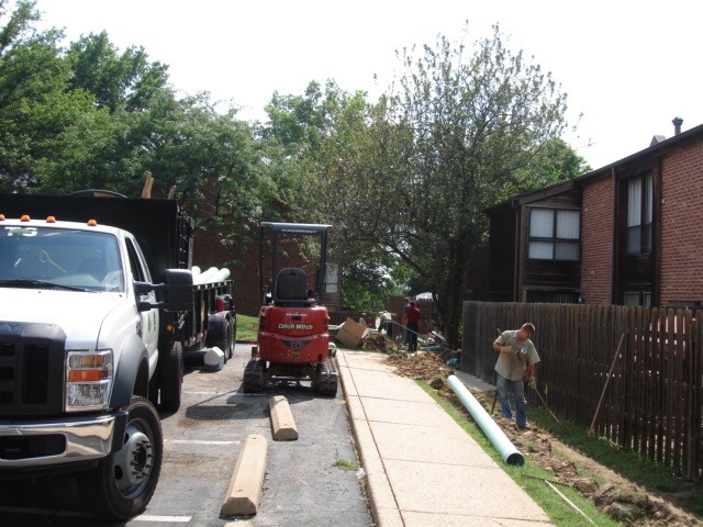 Construction crew digging trench beside apartment sidewalk