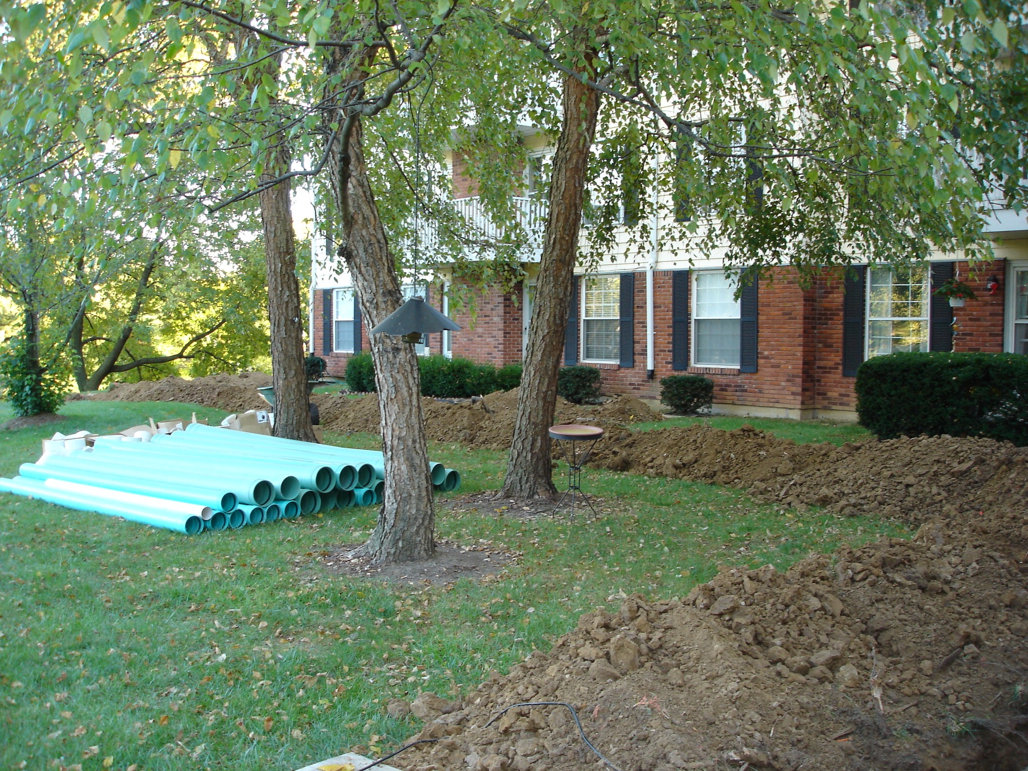 Trench and green pipes beside brick building