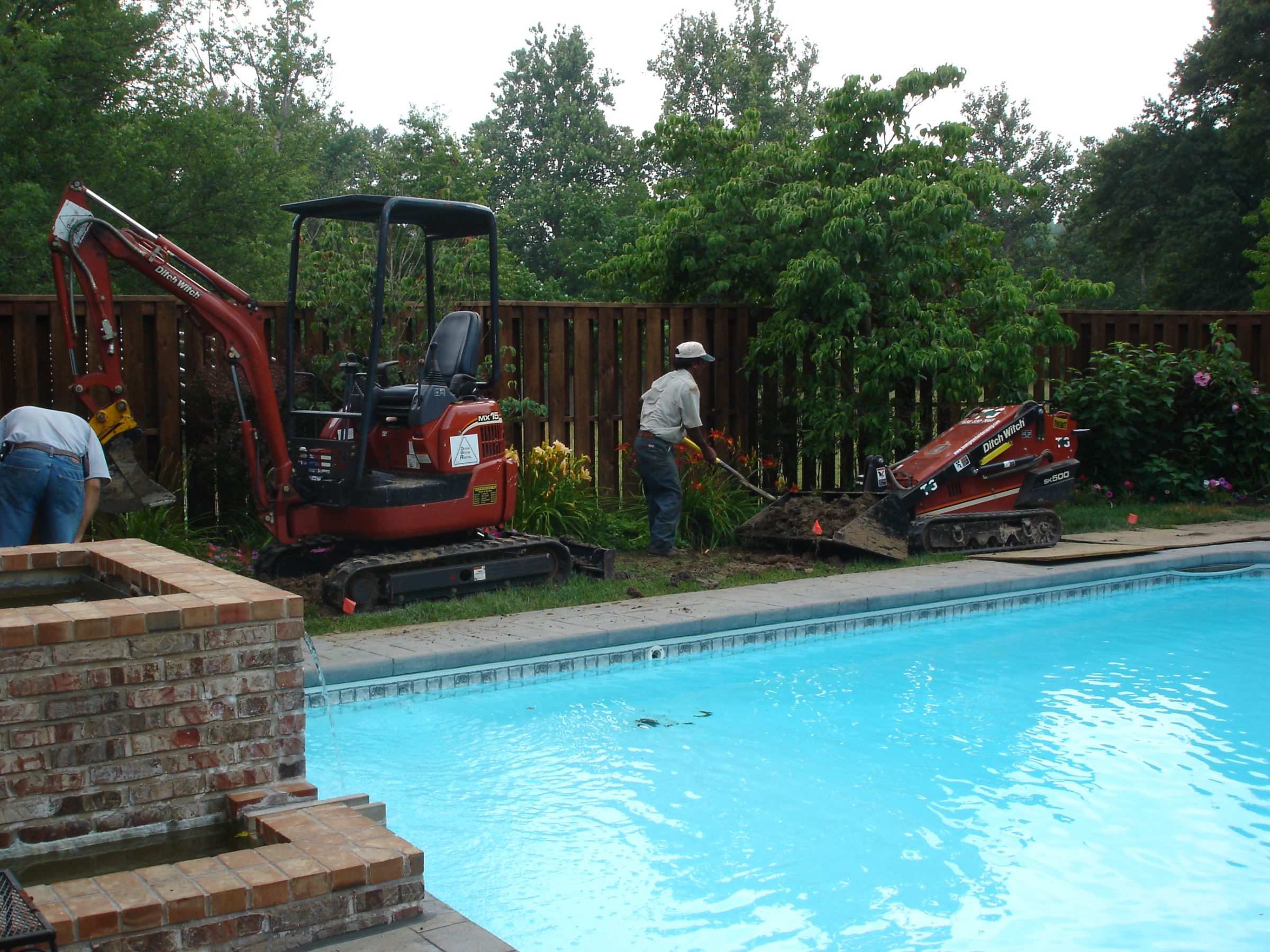 Workers excavating soil beside backyard swimming pool