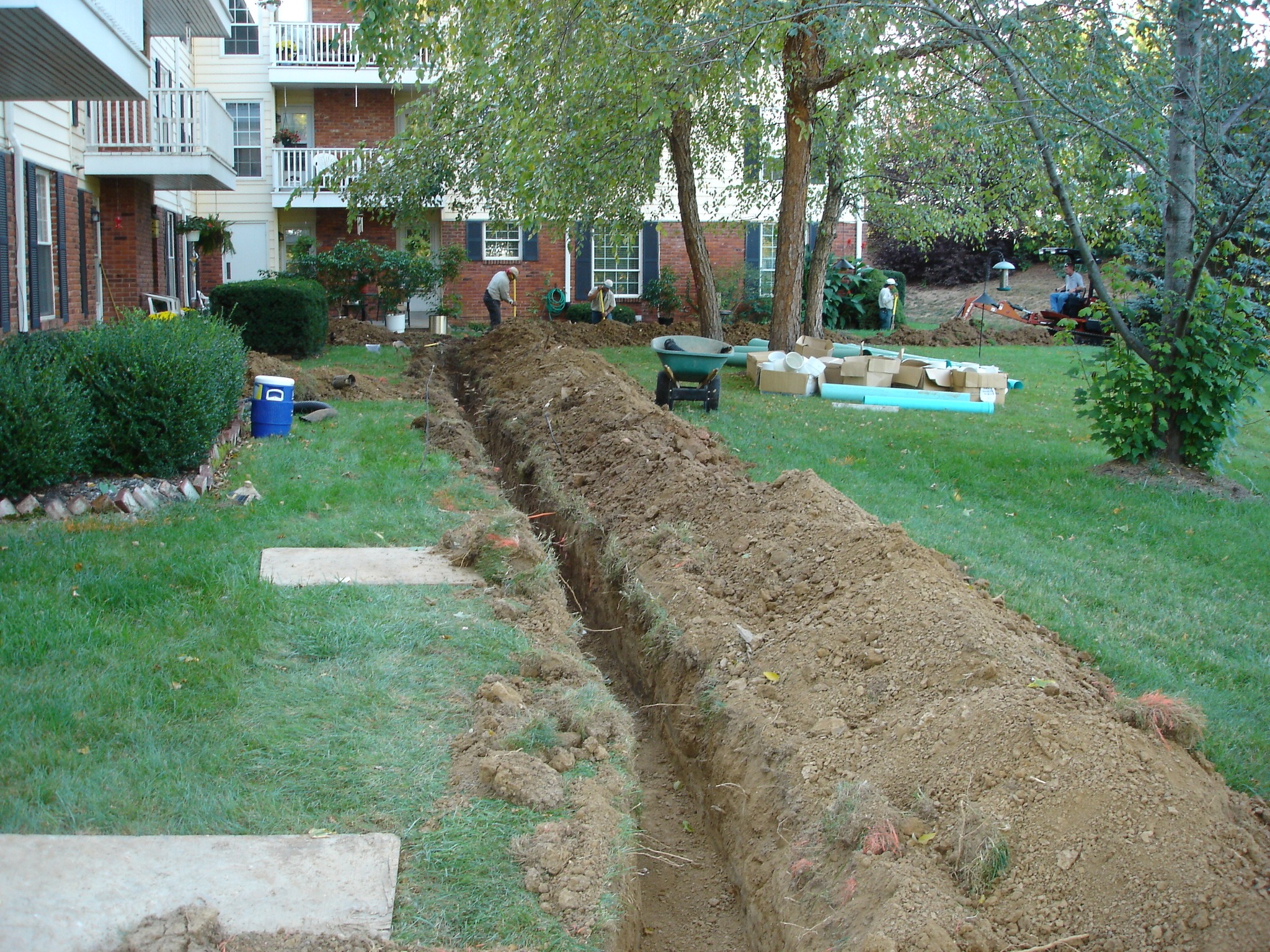 Workers digging trench for pipes near apartments