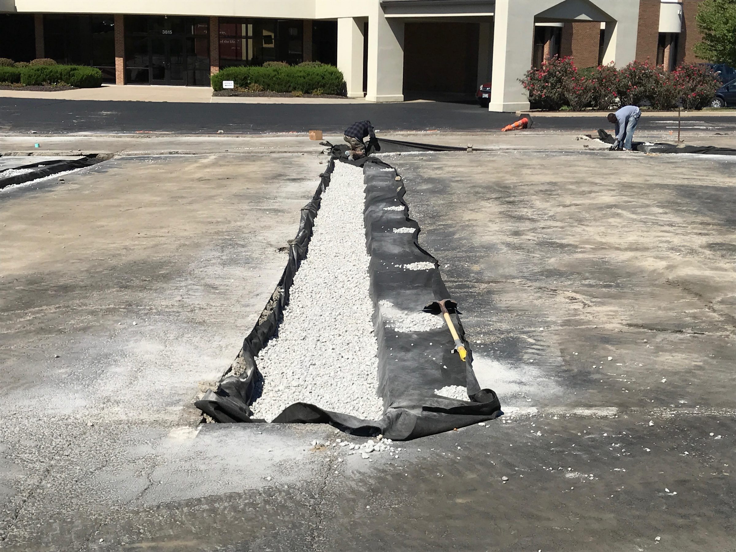Workers installing gravel drainage trench in parking lot