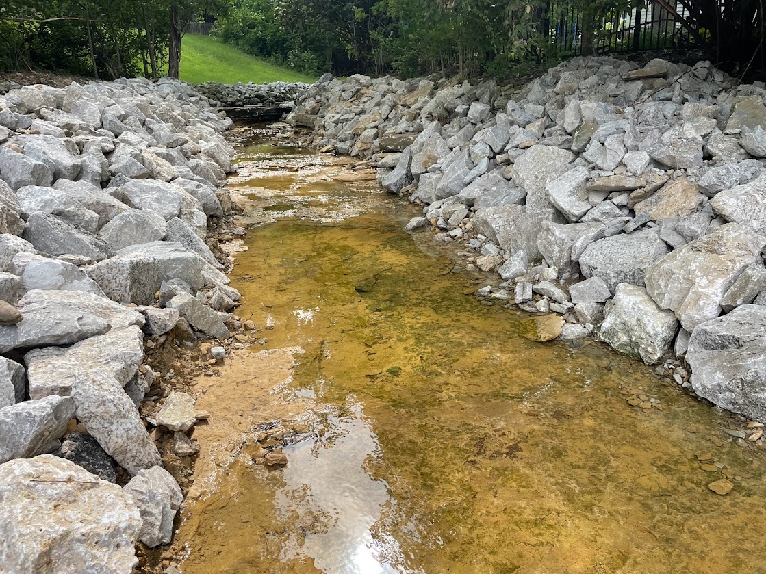 Shallow creek flowing between large gray rocks