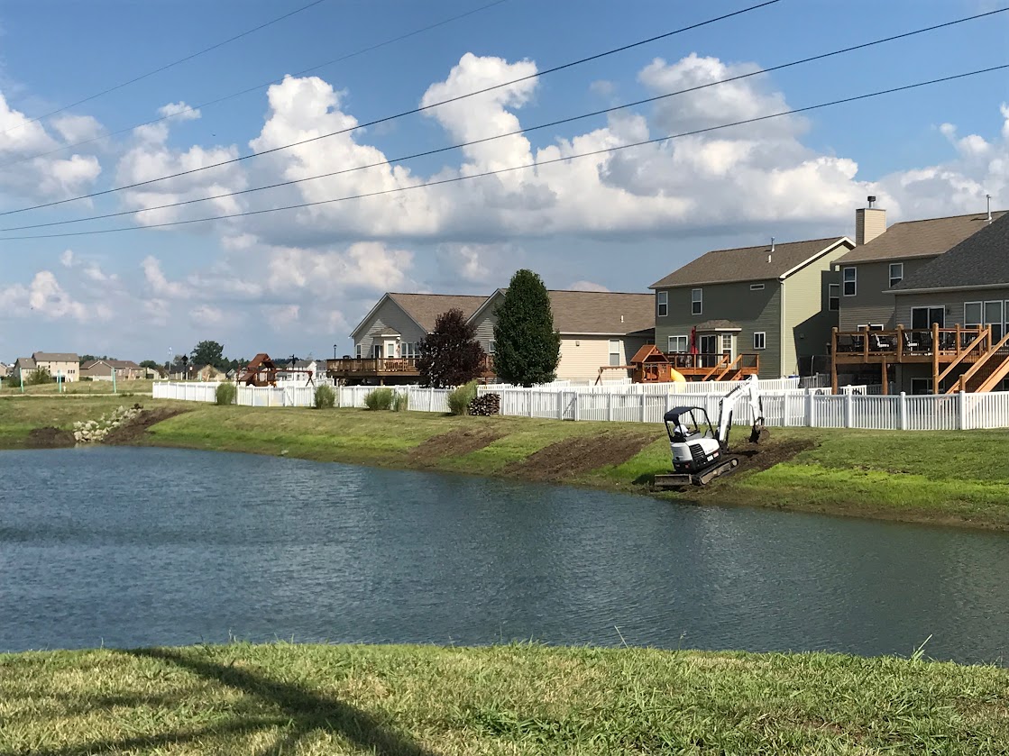 Excavator working beside suburban pond and houses