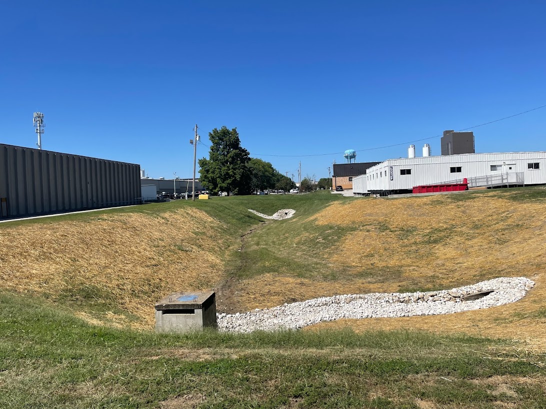 Grassy drainage ditch between industrial buildings