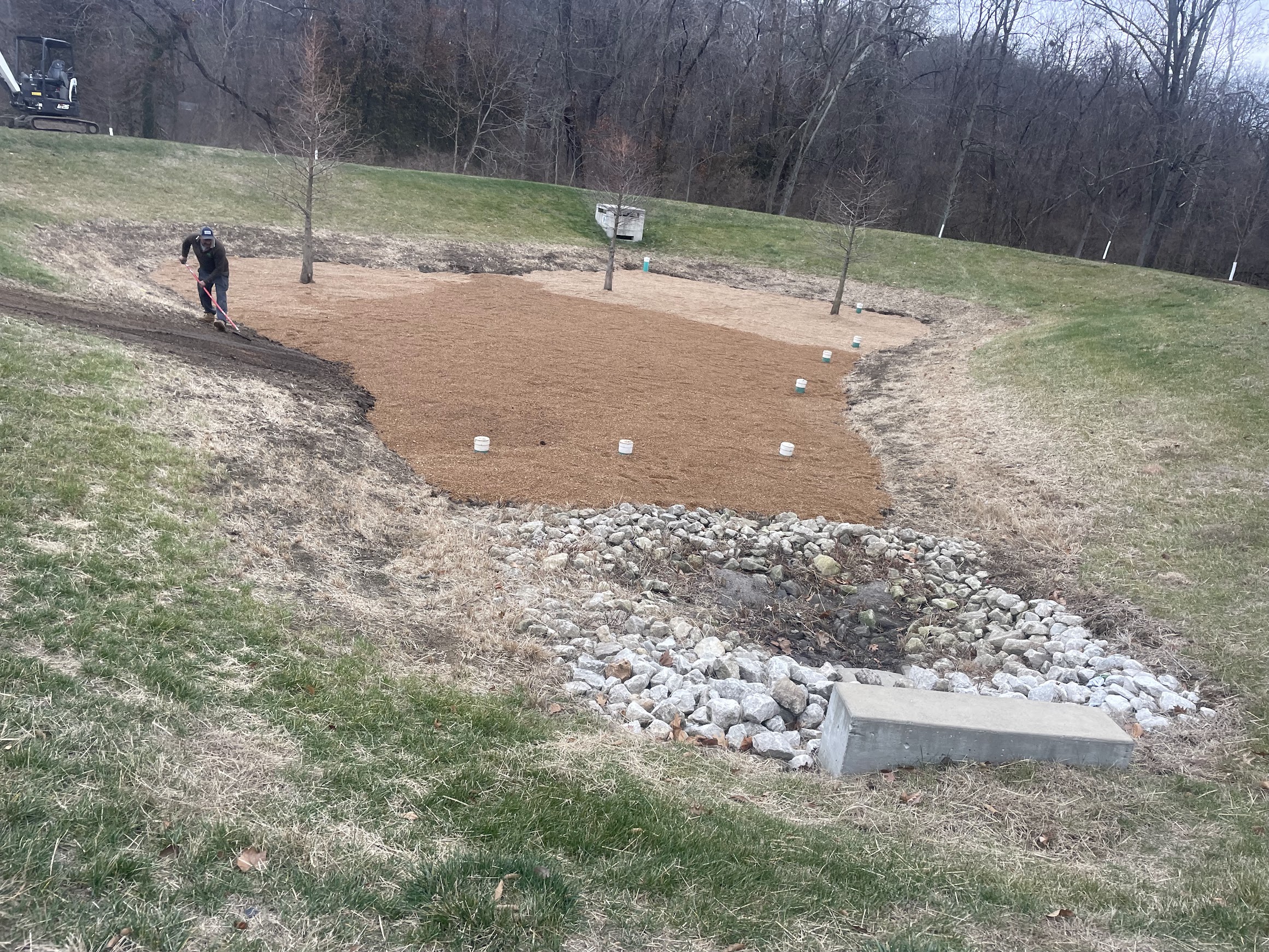 Worker raking soil in landscaped drainage basin