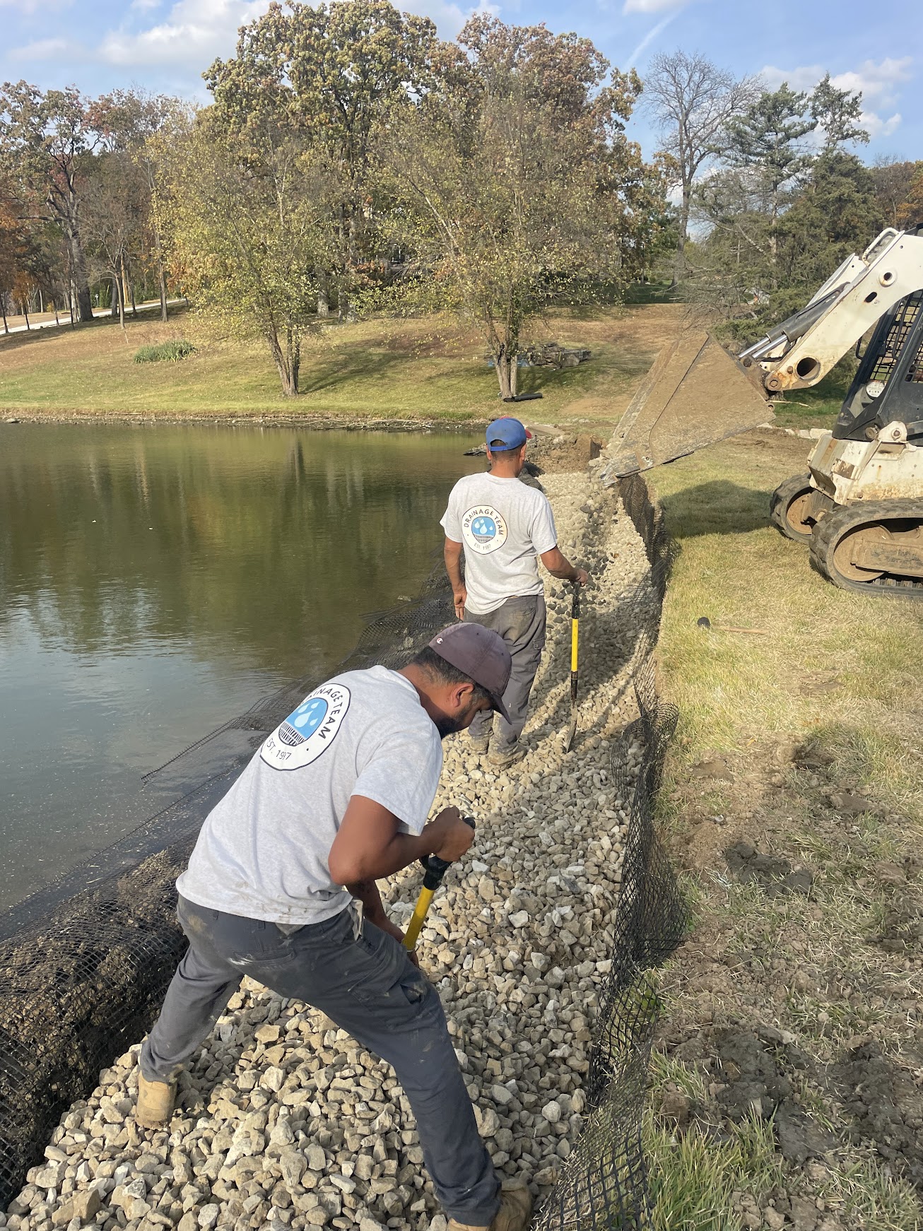 Workers installing rock shoreline reinforcement by pond