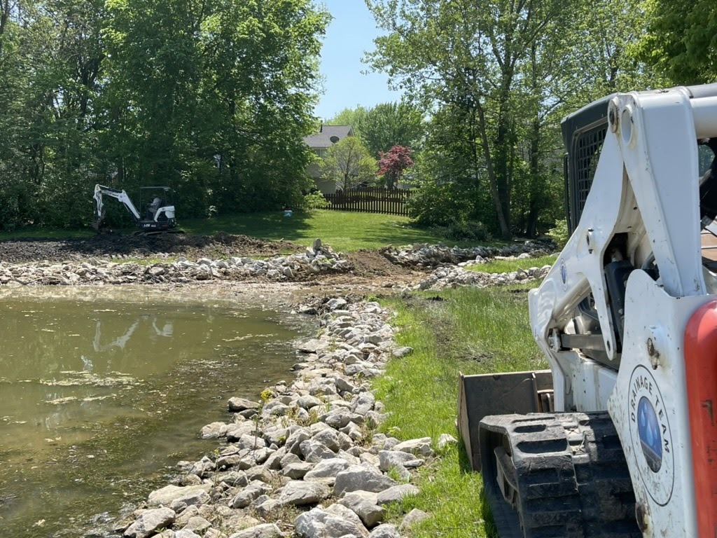 Excavators landscaping pond shoreline in backyard