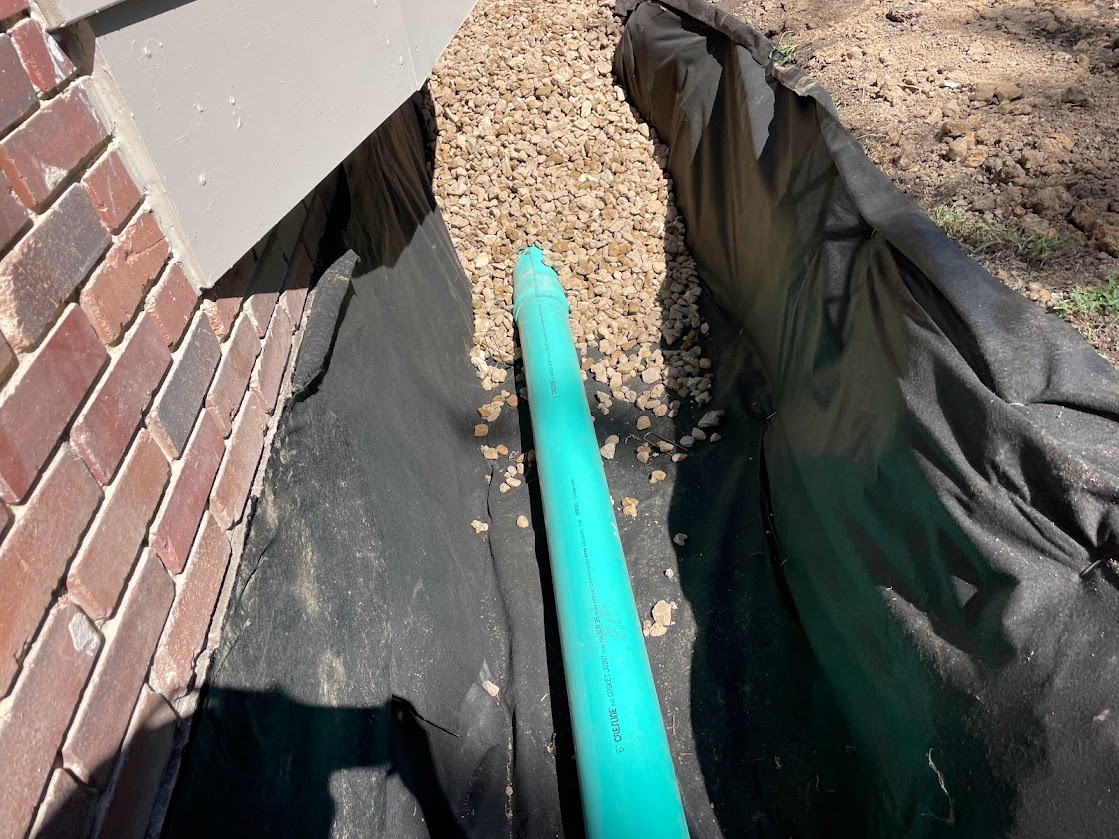Green PVC pipe in gravel trench beside house foundation